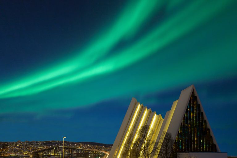 Illuminated Tromso cathedral at night with beautiful green shapes of aurora borealis